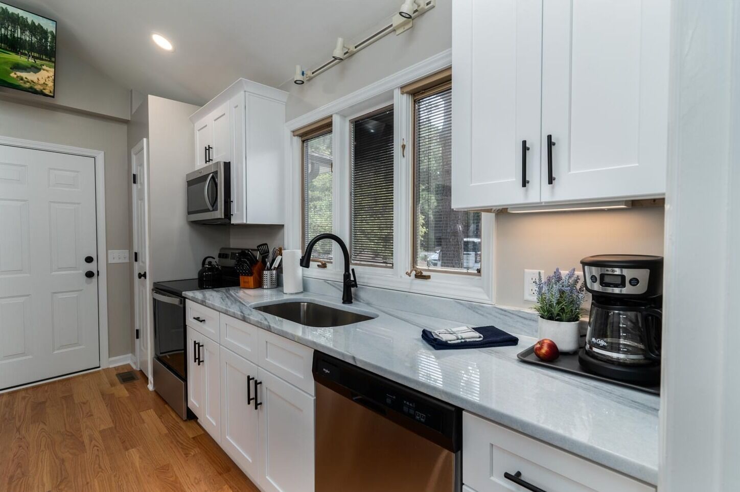 A modern kitchen with white cabinets, a stainless steel sink, a microwave, and a coffee maker.