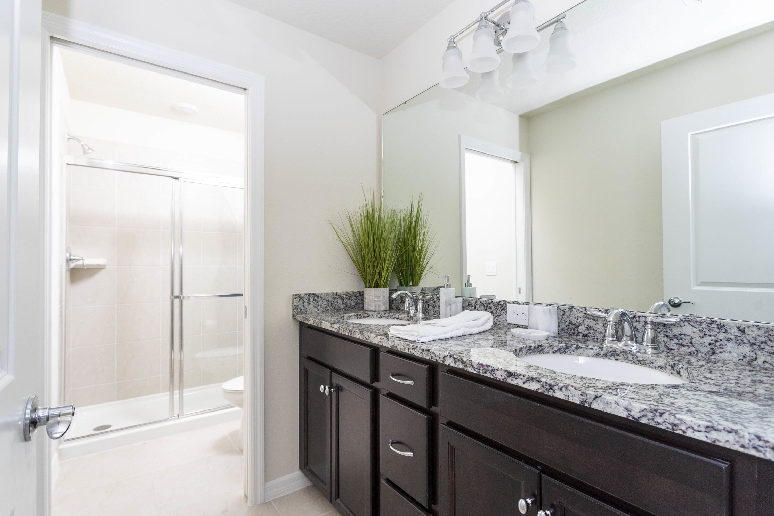 A modern bathroom with a glass shower enclosure, a marble sink, dark wooden cabinets, and a large mirror.