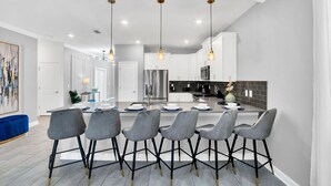 A modern kitchen with a central island, bar stools, pendant lighting, and a stainless steel refrigerator.