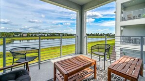 Un balcón con vistas a un lago y vegetación, con dos mesas y sillas de madera.