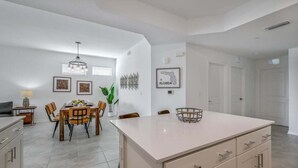 Una cocina moderna con una isla central, comedor con sillas y una mesa, y una lámpara colgante.
