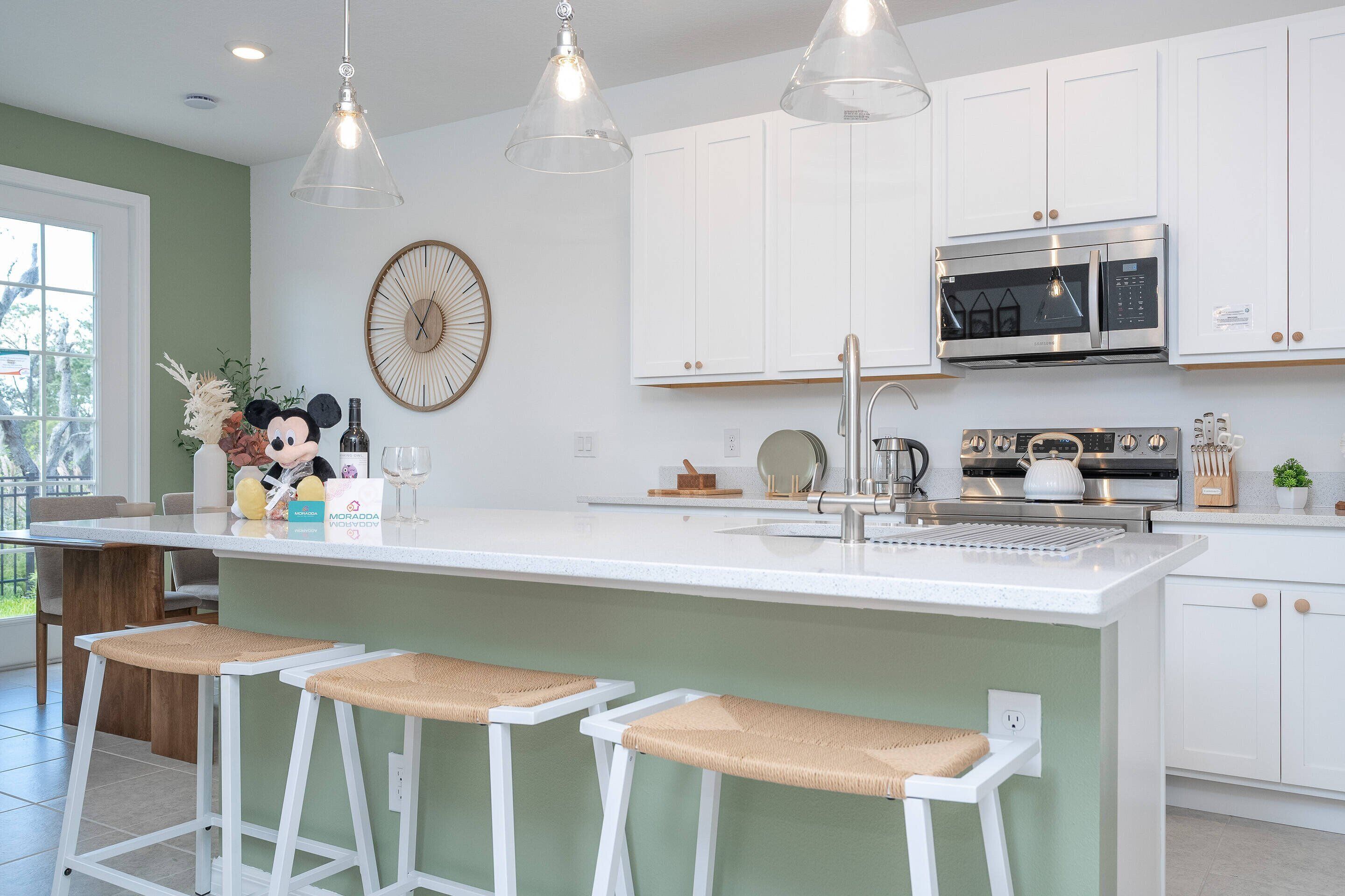 A modern kitchen with white cabinetry, a large island with bar stools, a microwave, and a sink.