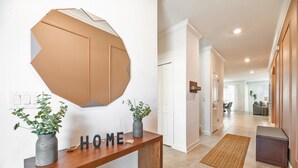 A modern hallway with a wooden console table, a geometric wall decoration, and a welcome sign.