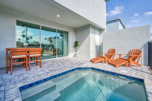 A modern outdoor pool area with a glass-enclosed patio, wooden chairs, and a small table. - Last Minute Disney Getaway! Private Pool & Themed Bedrooms. Book Now! #81943 (Orlando)