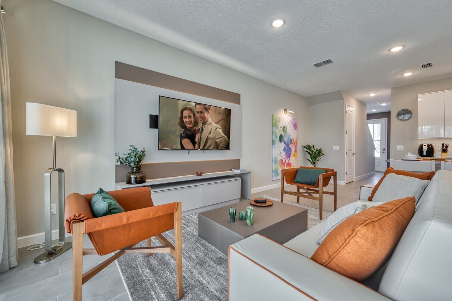 A modern living room with a sofa, armchairs, a coffee table, and a TV mounted on the wall.