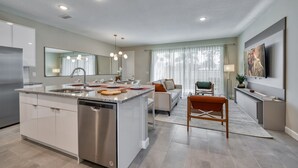 Cocina moderna con una isla central, electrodomésticos de acero inoxidable y un área de comedor con sofá y sillas.