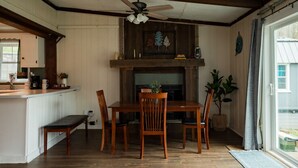A dining area with a wooden table and chairs, a ceiling fan, and a view of the outdoors through a window.