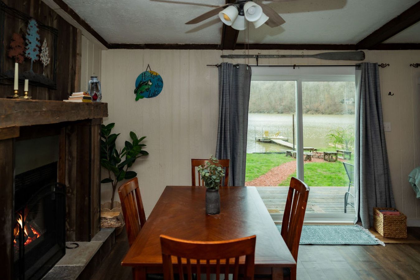 Un espace repas avec une table et des chaises en bois, une cheminée et une vue sur un lac, visible à travers de grandes portes-fenêtres coulissantes.