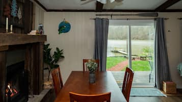 A dining area with a wooden table and chairs, a fireplace, and a view of a lake through large sliding glass doors.