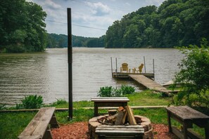A lakeside dock with two chairs and a table, surrounded by greenery and a fire pit. - lake front cabin hot tub peaceful stunning views (Martinsville)