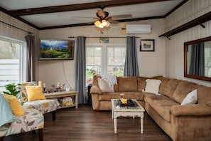 A cozy living room with a brown sofa, a small white coffee table, a floral armchair, and a ceiling fan.