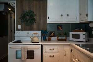 A kitchen with a stove, kettle, microwave, and cabinets.