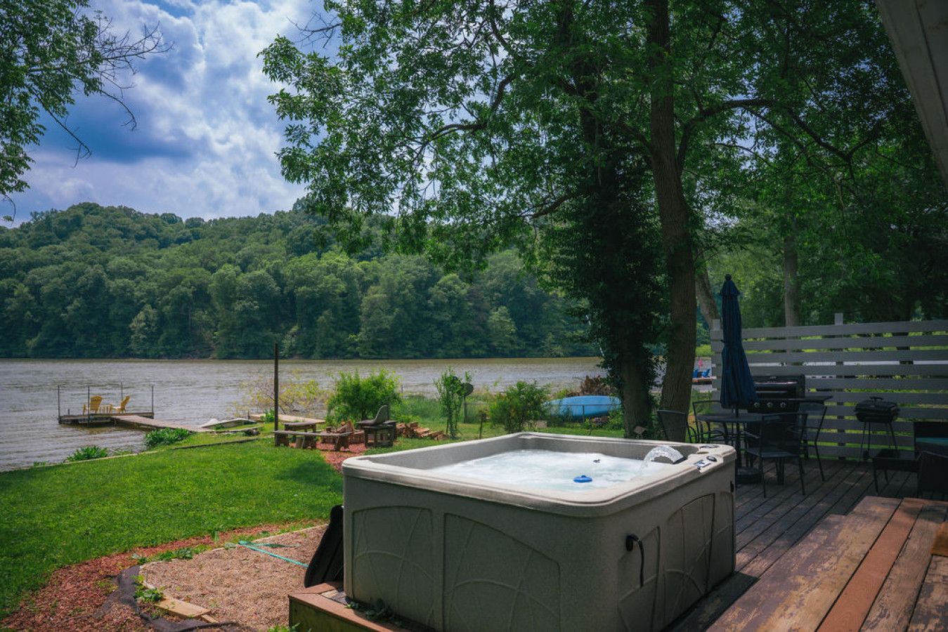 A hot tub on a deck with a lake view, surrounded by a wooden deck and outdoor furniture.