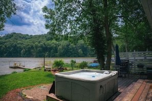 A hot tub on a deck with a lake view, surrounded by a wooden deck and outdoor furniture.