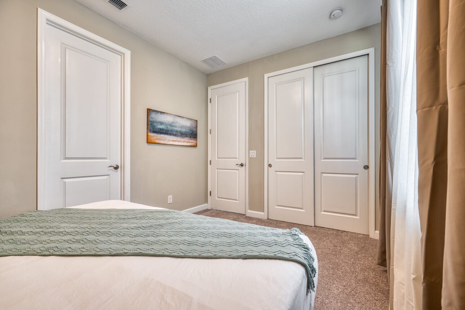 A bedroom with a bed, a painting on the wall, and a set of white doors.