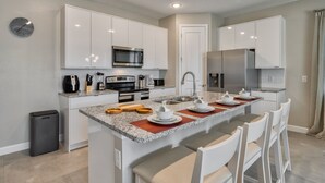 A modern kitchen with white cabinets, a granite countertop, stainless steel appliances, and a dining area with white chairs.