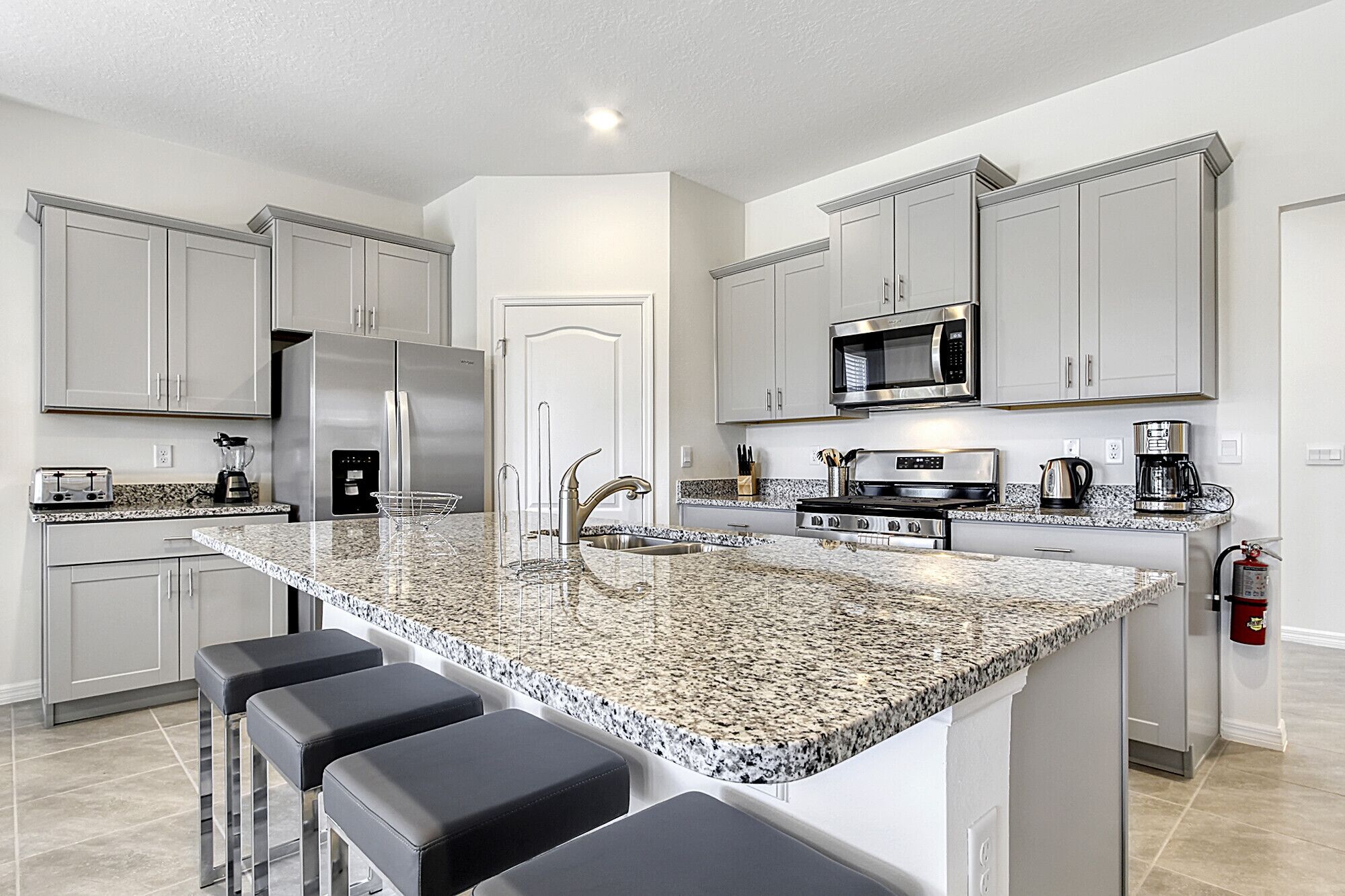 Una cocina moderna con encimeras de granito, electrodomésticos de acero inoxidable y una isla central con taburetes de bar.