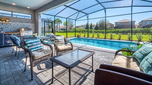 Un espace extérieur abrité comprenant une piscine, des meubles en osier et un barbecue.
