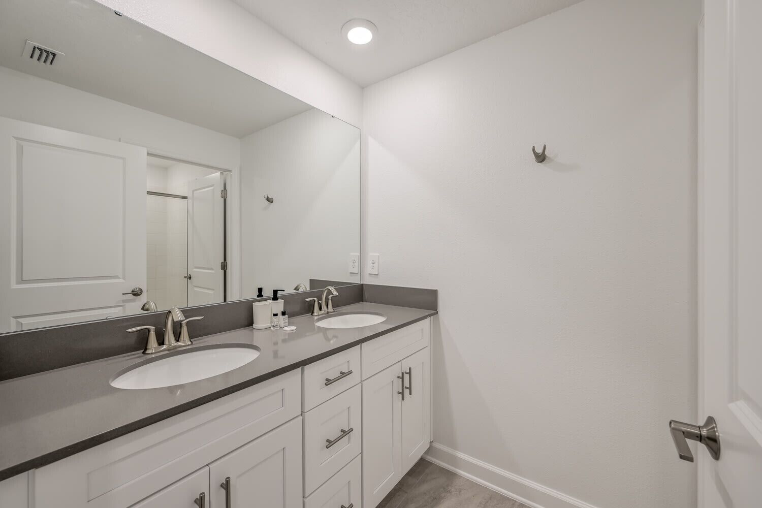 A modern bathroom with two sinks, a large mirror, and a door with a handle.