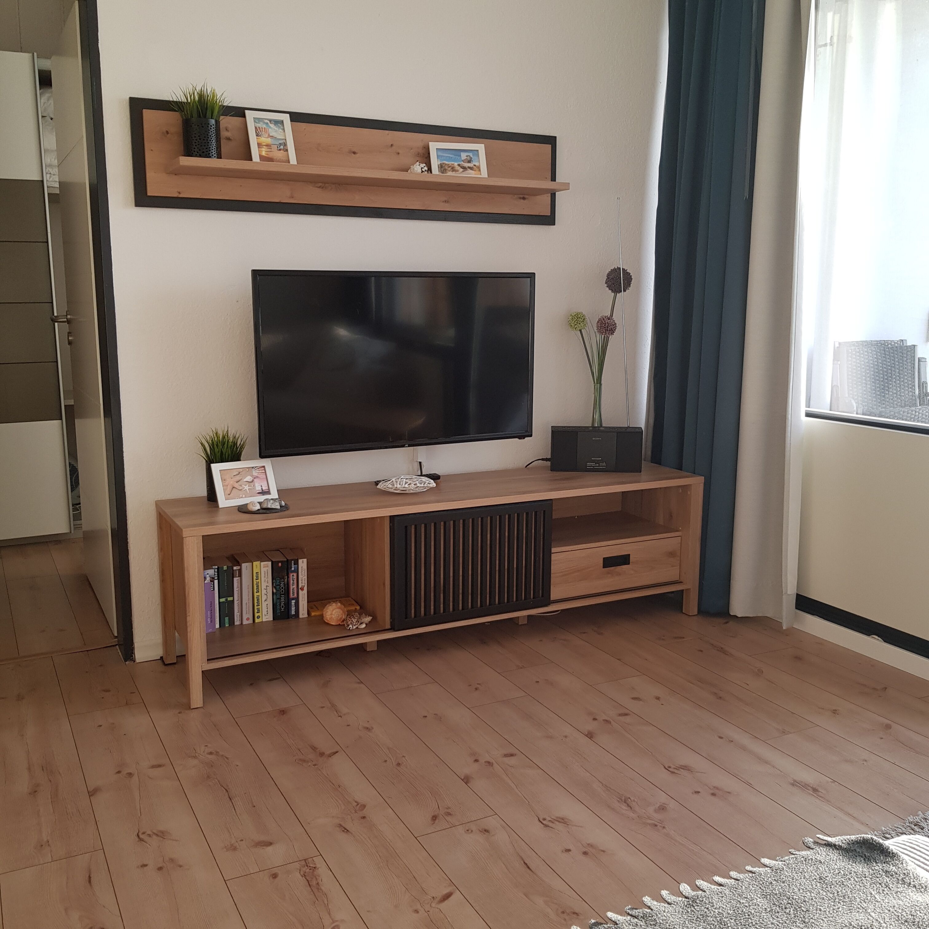 Olohuoneessa on puinen mediakeskus, litteänäyttöinen televisio ja ikkuna, jossa on verhot.