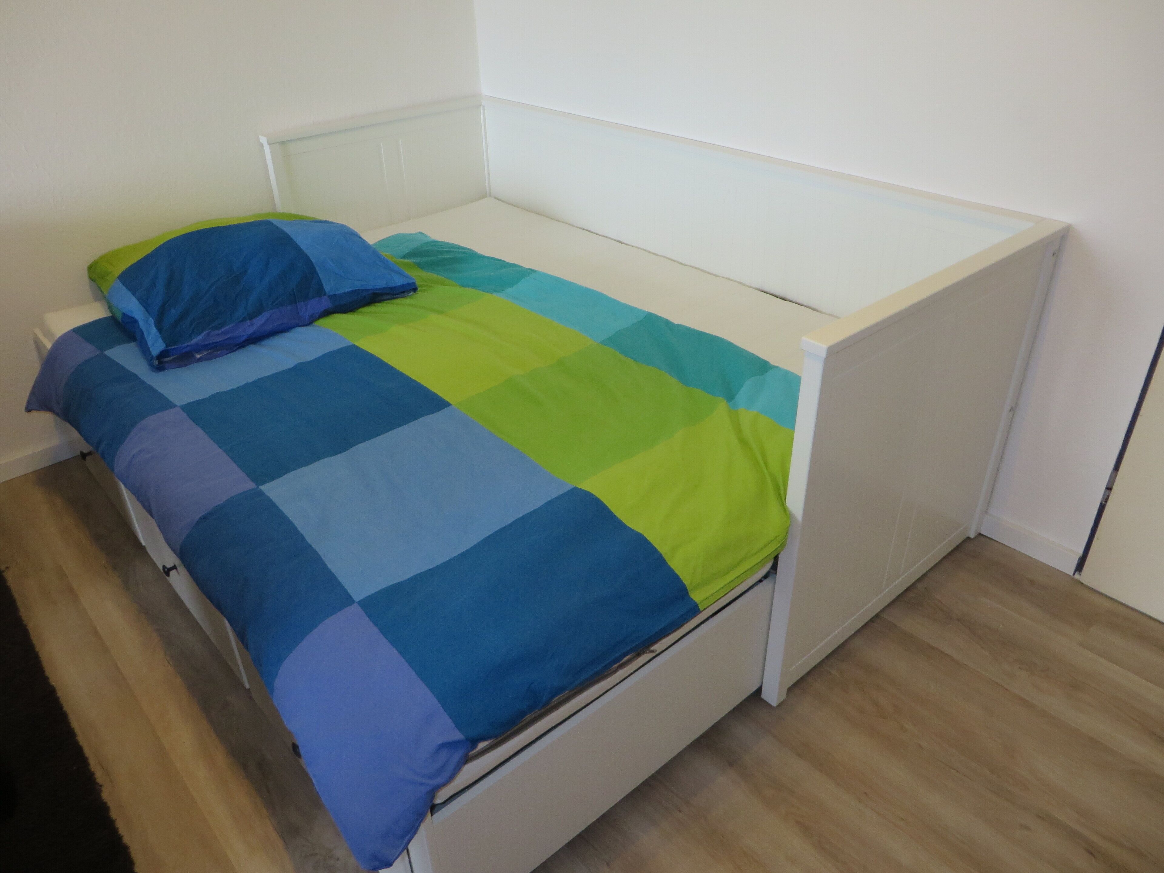 A single bed with a blue and green checkered bedspread and a matching pillow.