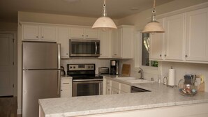 Una cocina moderna con armarios blancos, electrodomésticos de acero inoxidable, encimera de mármol e iluminación colgante.
