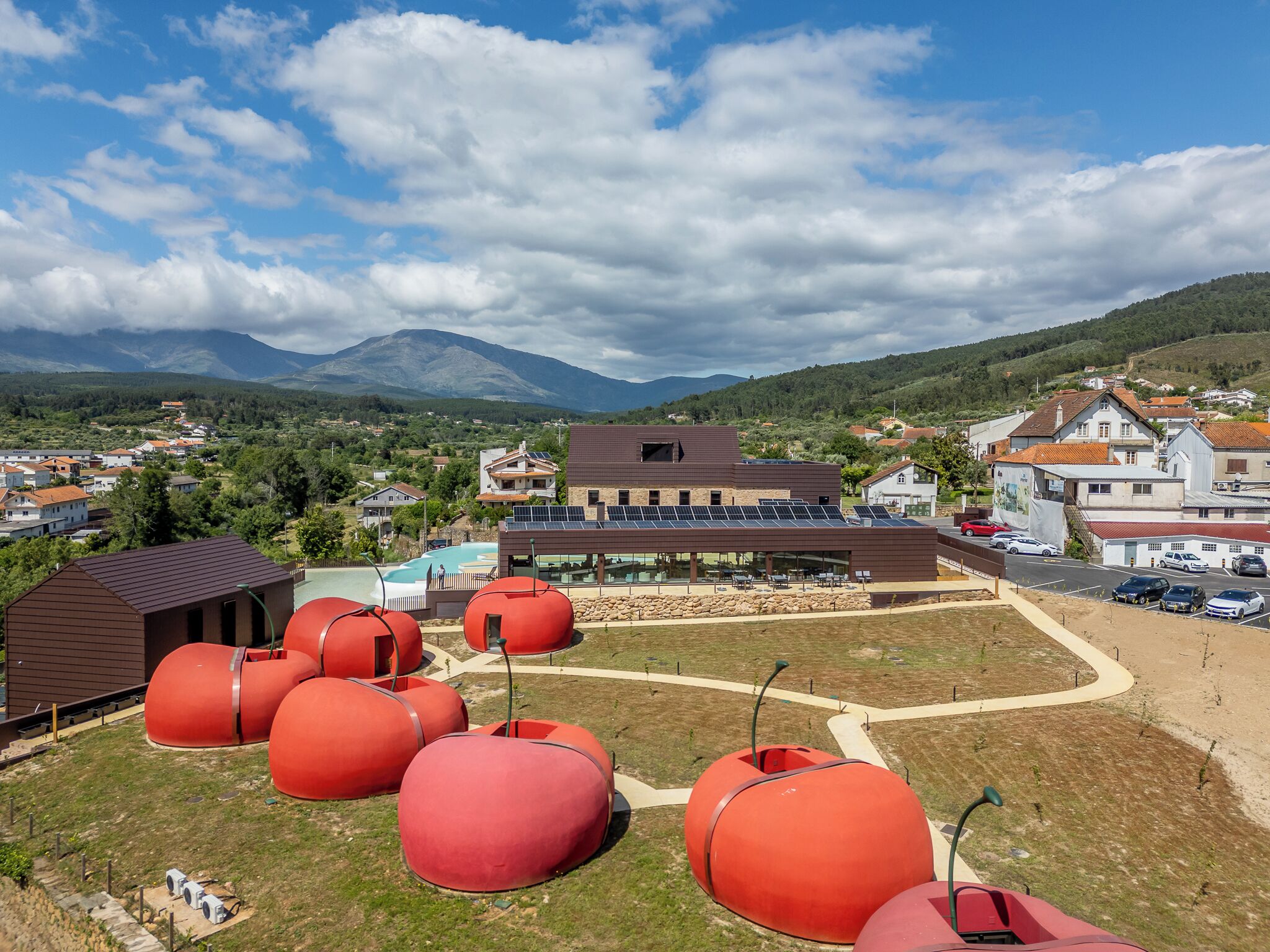 A modern building with a flat roof and solar panels, surrounded by a parking area and red spherical structures.