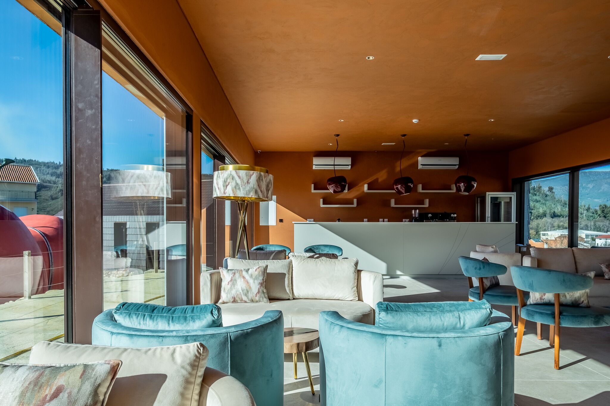 Een moderne woonkamer met een gebogen bank, blauwe fauteuils en een keuken met witte kasten en een groot raam.