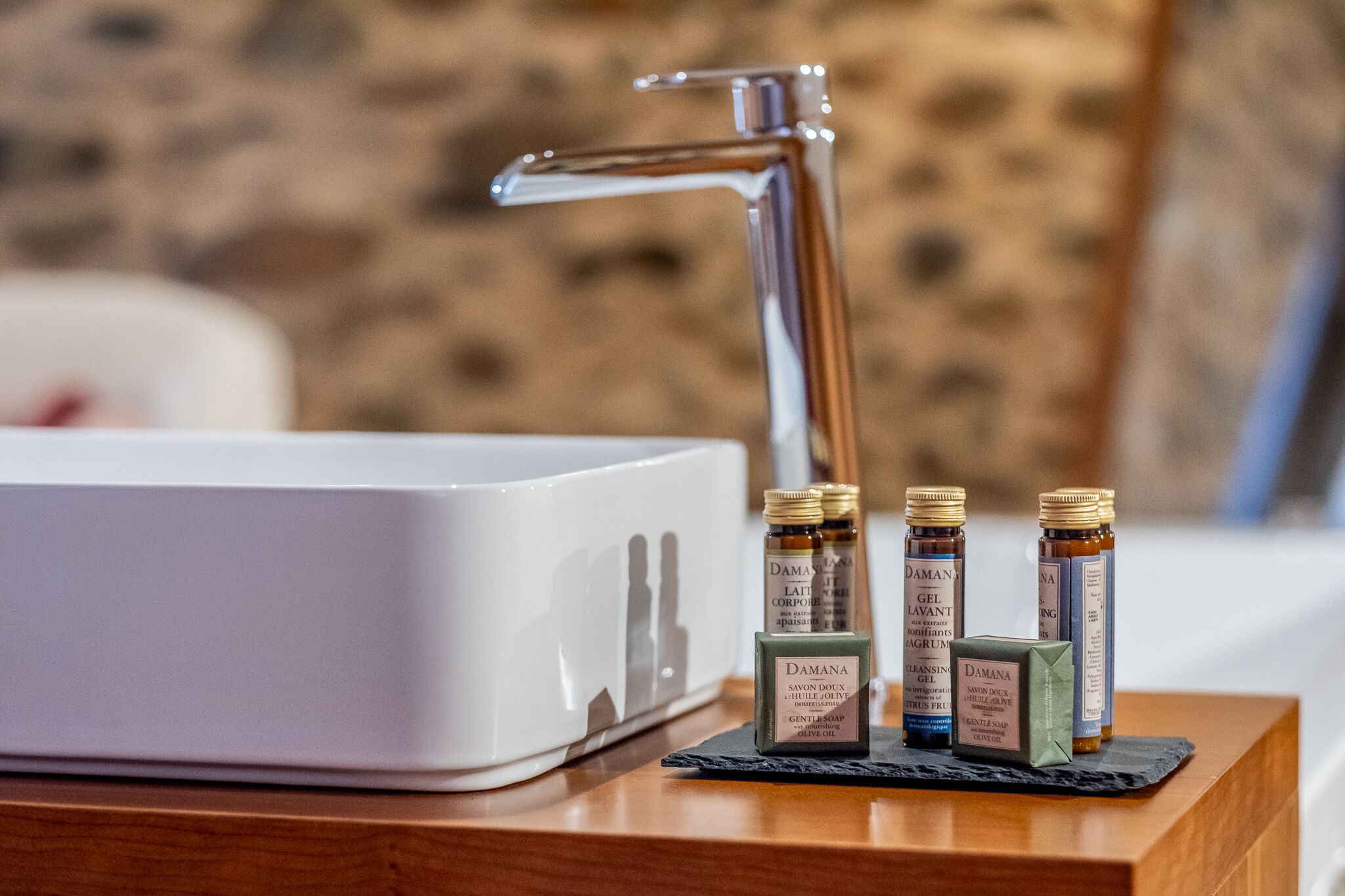 Un lavabo de salle de bain avec trois bouteilles de savon Damana disposées sur un plateau en bois.