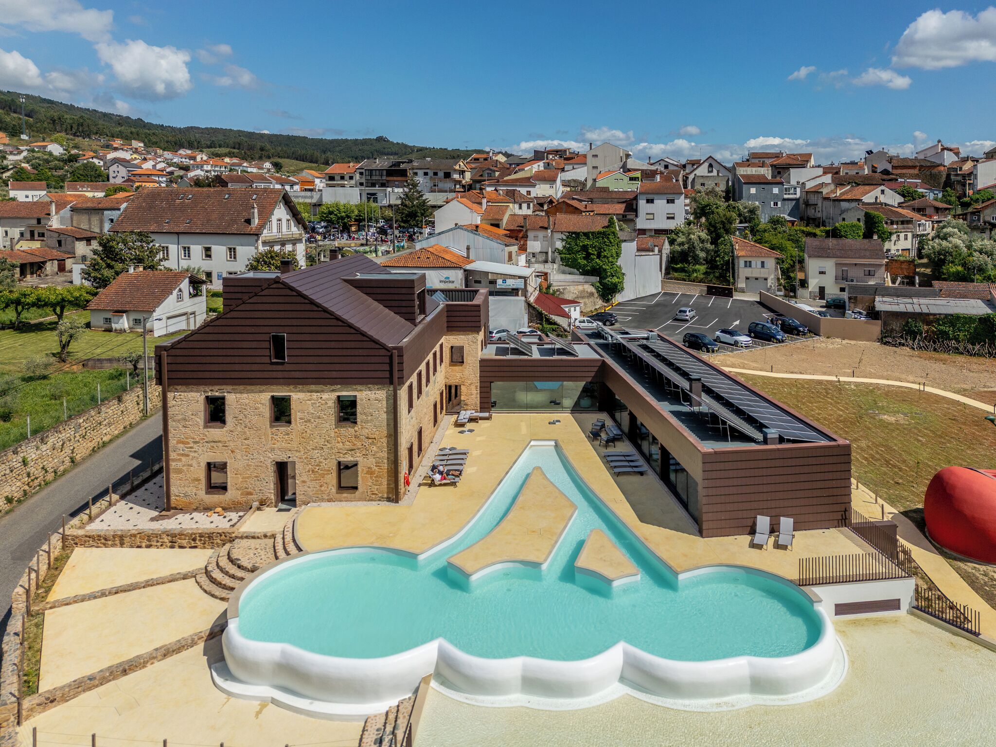 A hotel with a swimming pool, a parking area, and a view of a residential area.