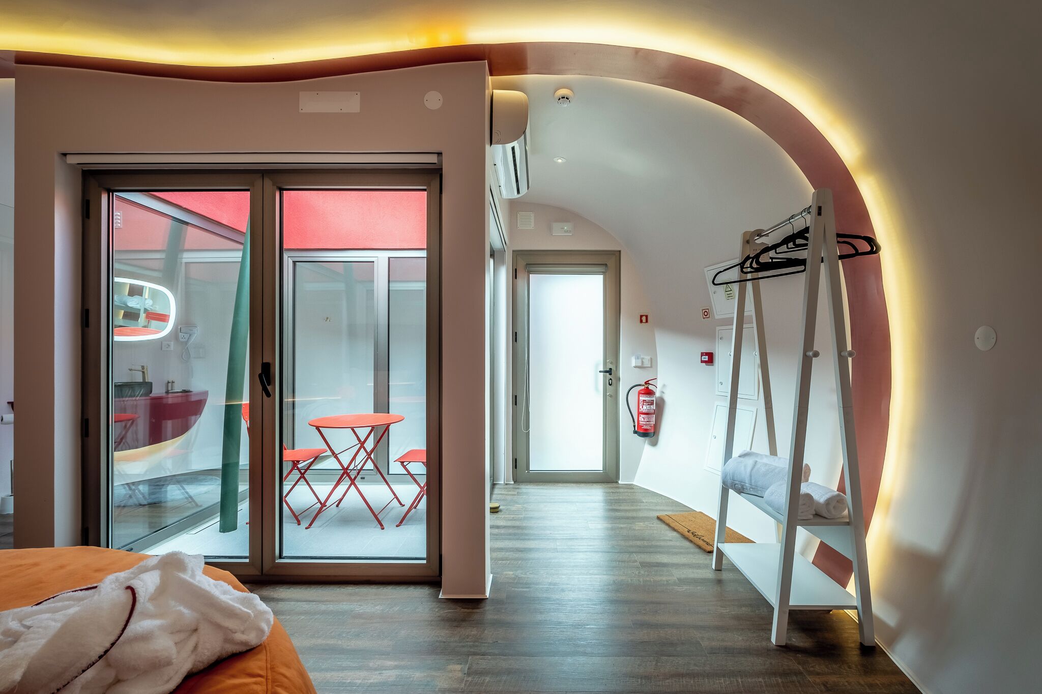 Ein modernes Hotelzimmer mit einer Schiebetür zu einem Balkon, einem kleinen Tisch mit Stühlen, einem Etagenbett und einem an der Wand befestigten Wäscheständer.