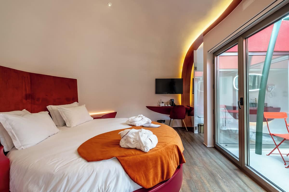 Et moderne hotelværelse med en stor seng, et fjernsyn og en skydedør til et udendørs område.