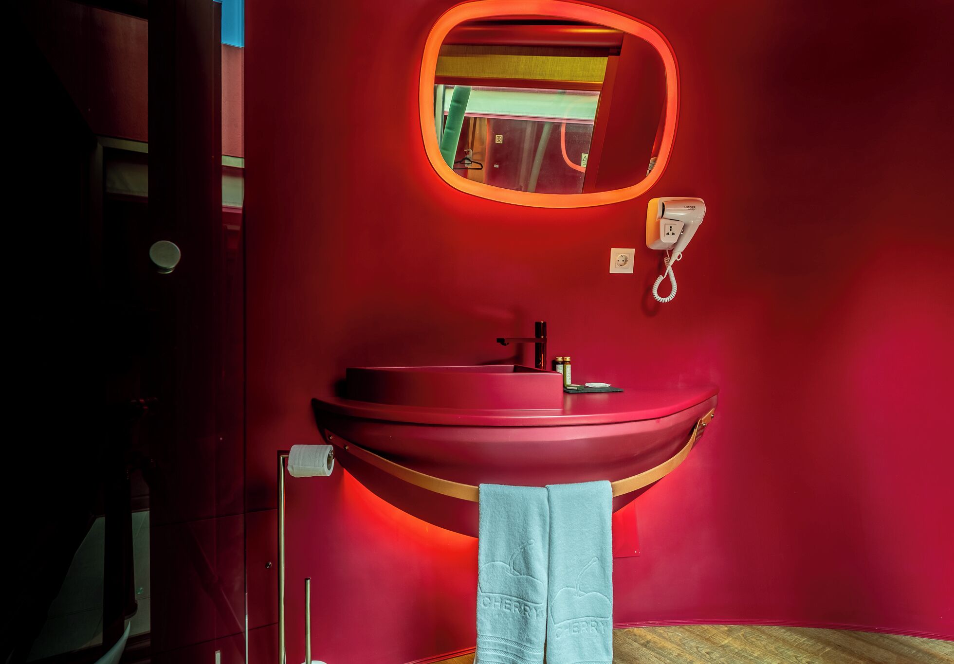 A red bathroom with a round mirror, a red sink, and a towel hanging on the wall.