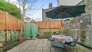 A patio with a table and chairs, a green umbrella, and a brick wall. - Stylish Central 2-bed Apartment With Pvt Garden (London)
