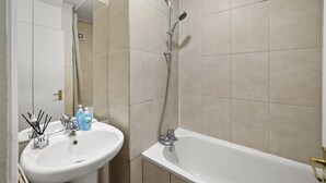 A bathroom with a white sink, a mirror, and a bathtub. - Stylish Central 2-bed Apartment With Pvt Garden (London)