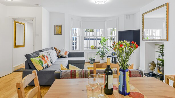 A modern living room with a sofa, dining table, and a TV. - Stylish Central 2-bed Apartment With Pvt Garden (London)