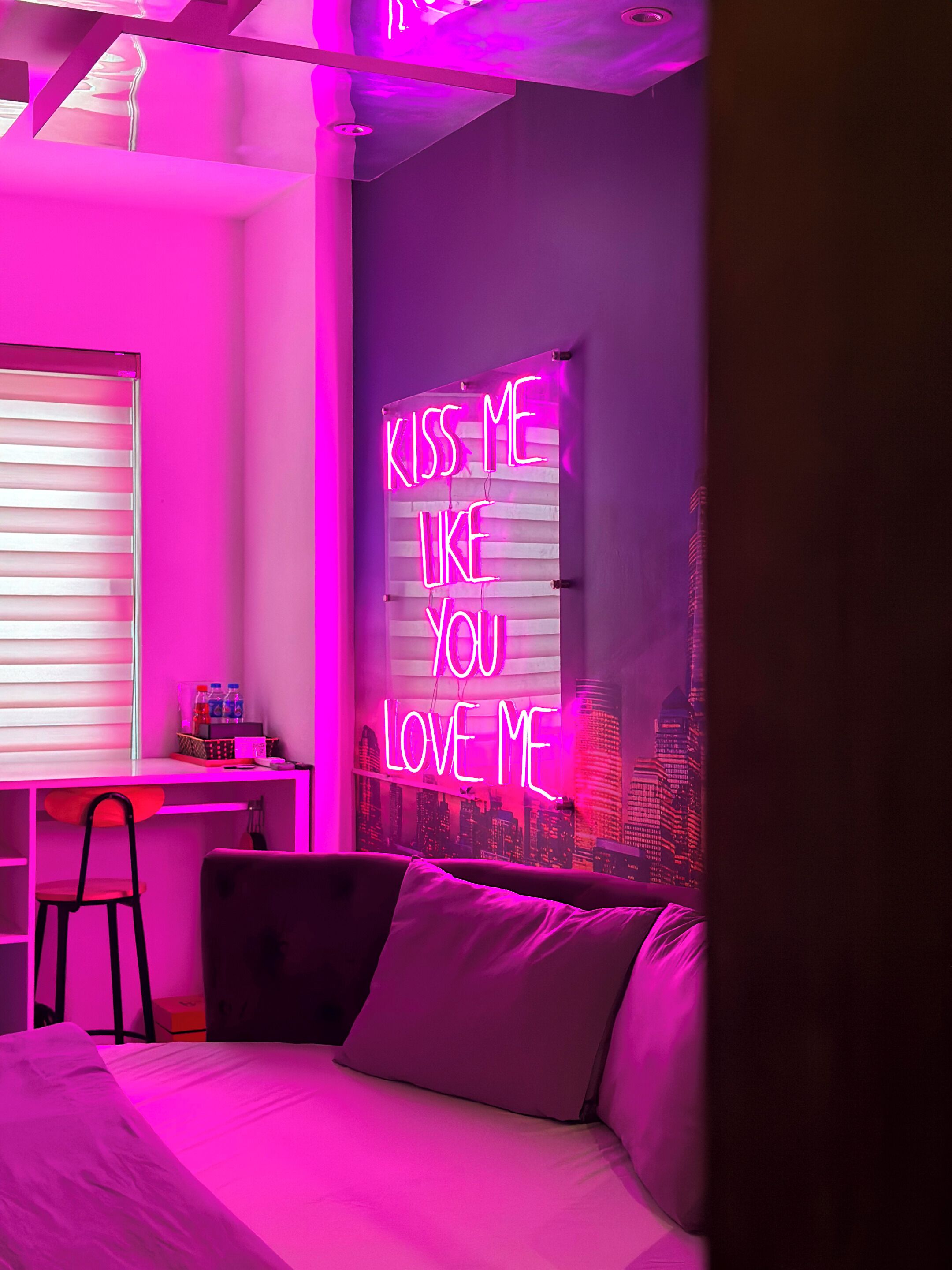 Una habitación con un letrero de neón que dice "KISS ME LIKE YOU LOVE ME" en la pared.