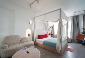 A bedroom with a four-poster bed, a sofa, a small round table with a remote control, and a chair. - 69 Boutique Hotel (Hanoi)