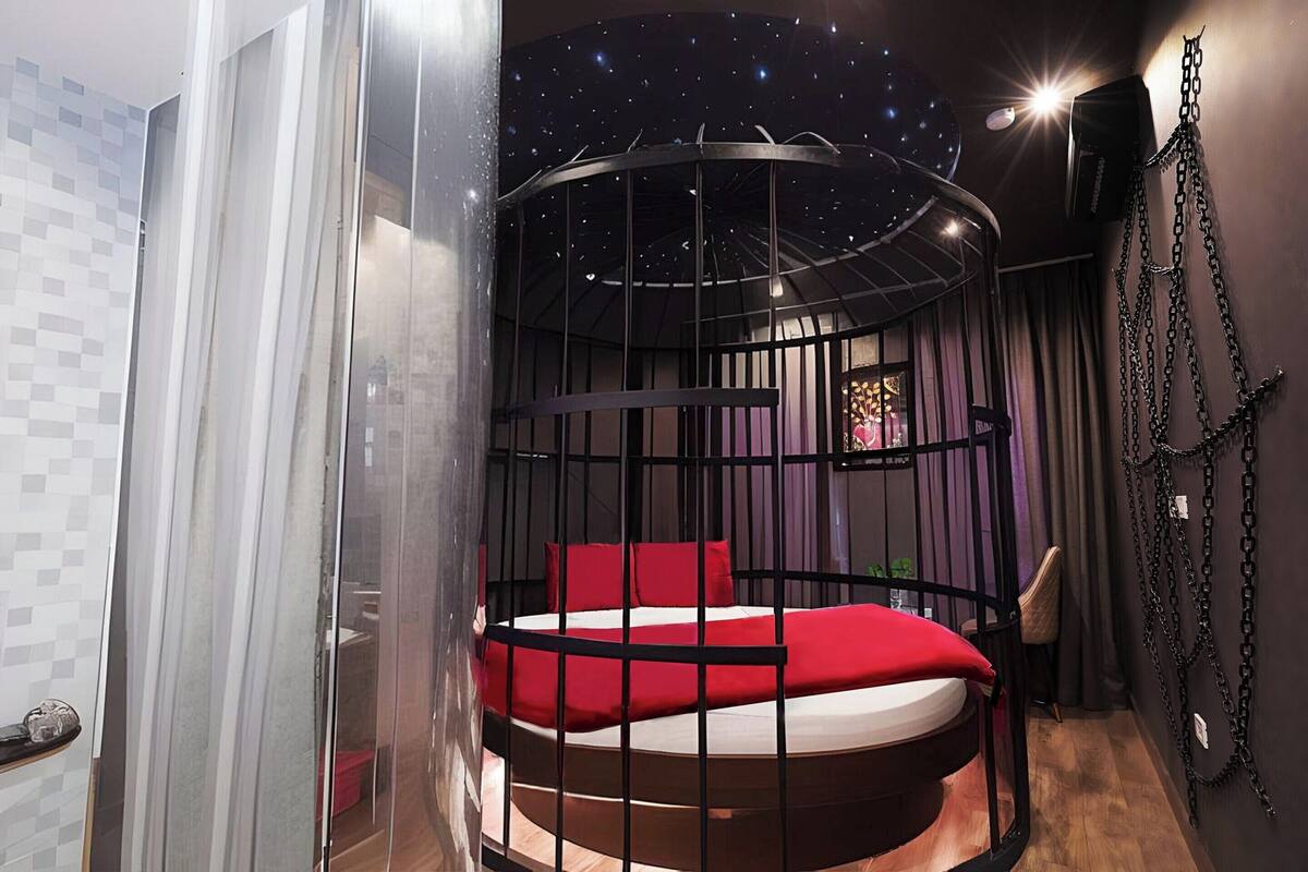 A circular bed with a red mattress and black metal frame, surrounded by a glass enclosure.