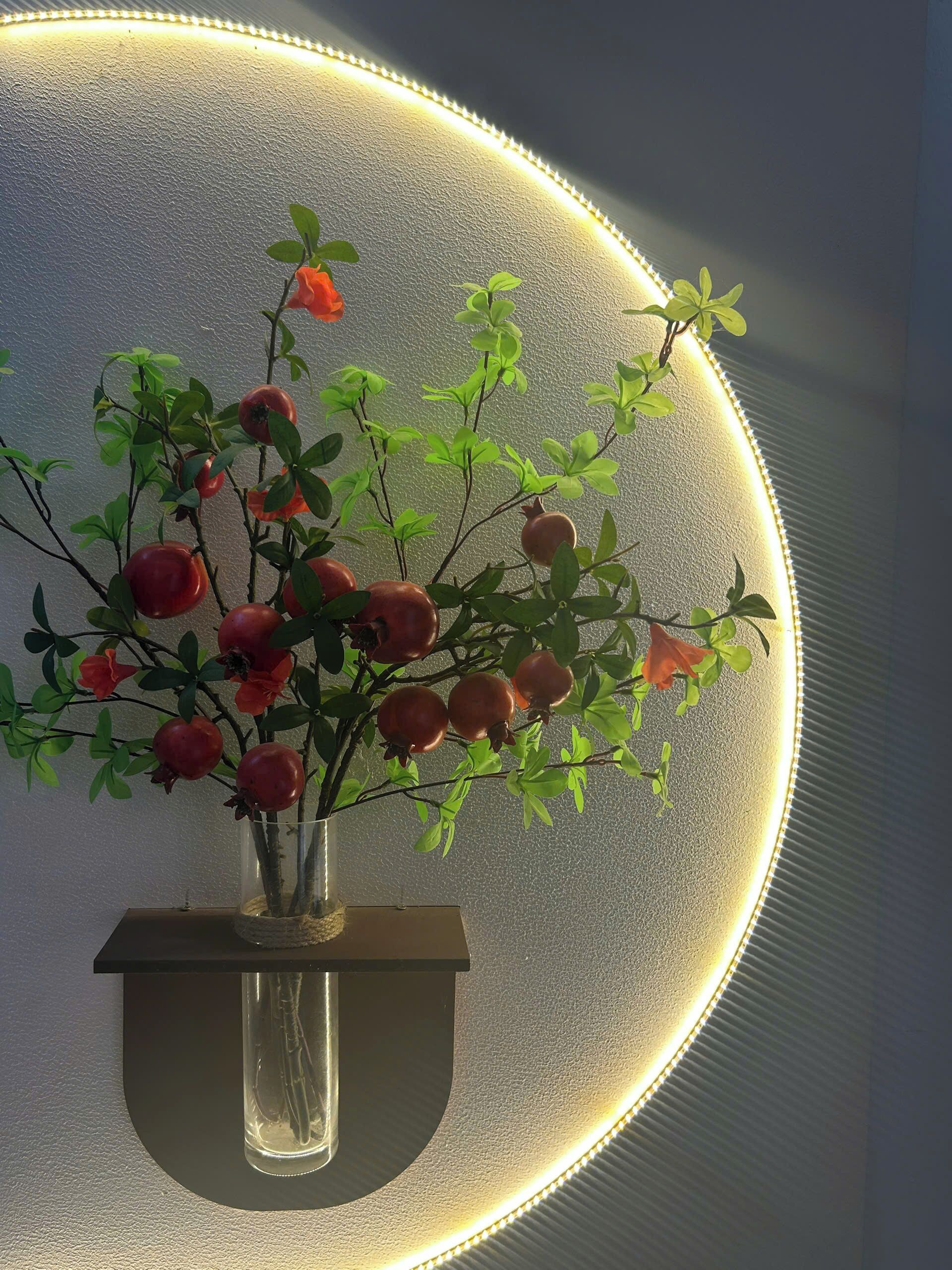 Een bloeiende kamerplant met rode bloemen en groene bladeren op een wandplank.