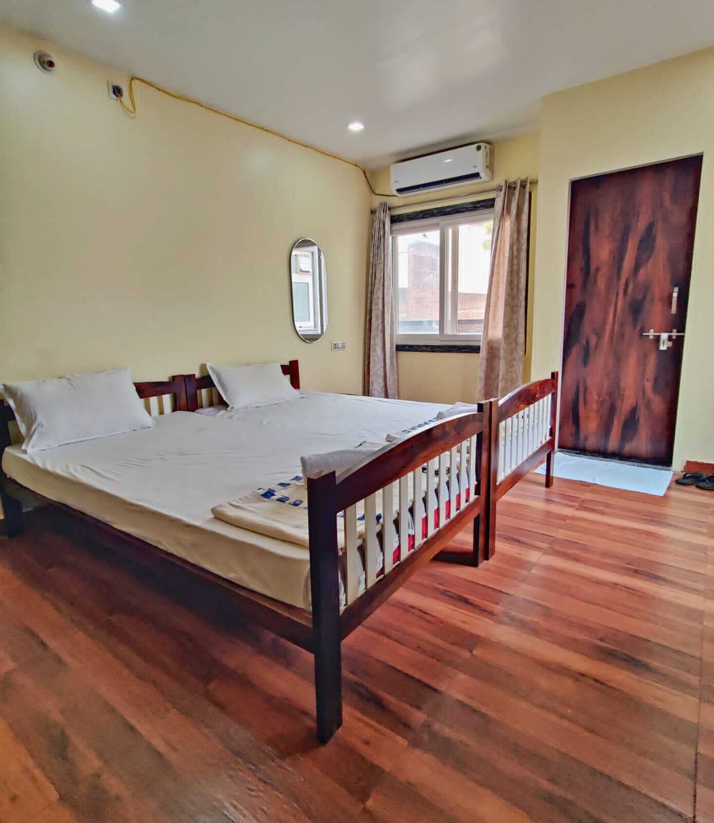 Een slaapkamer met een houten bed, een raam met gordijnen, een airconditioning en een houten deur.