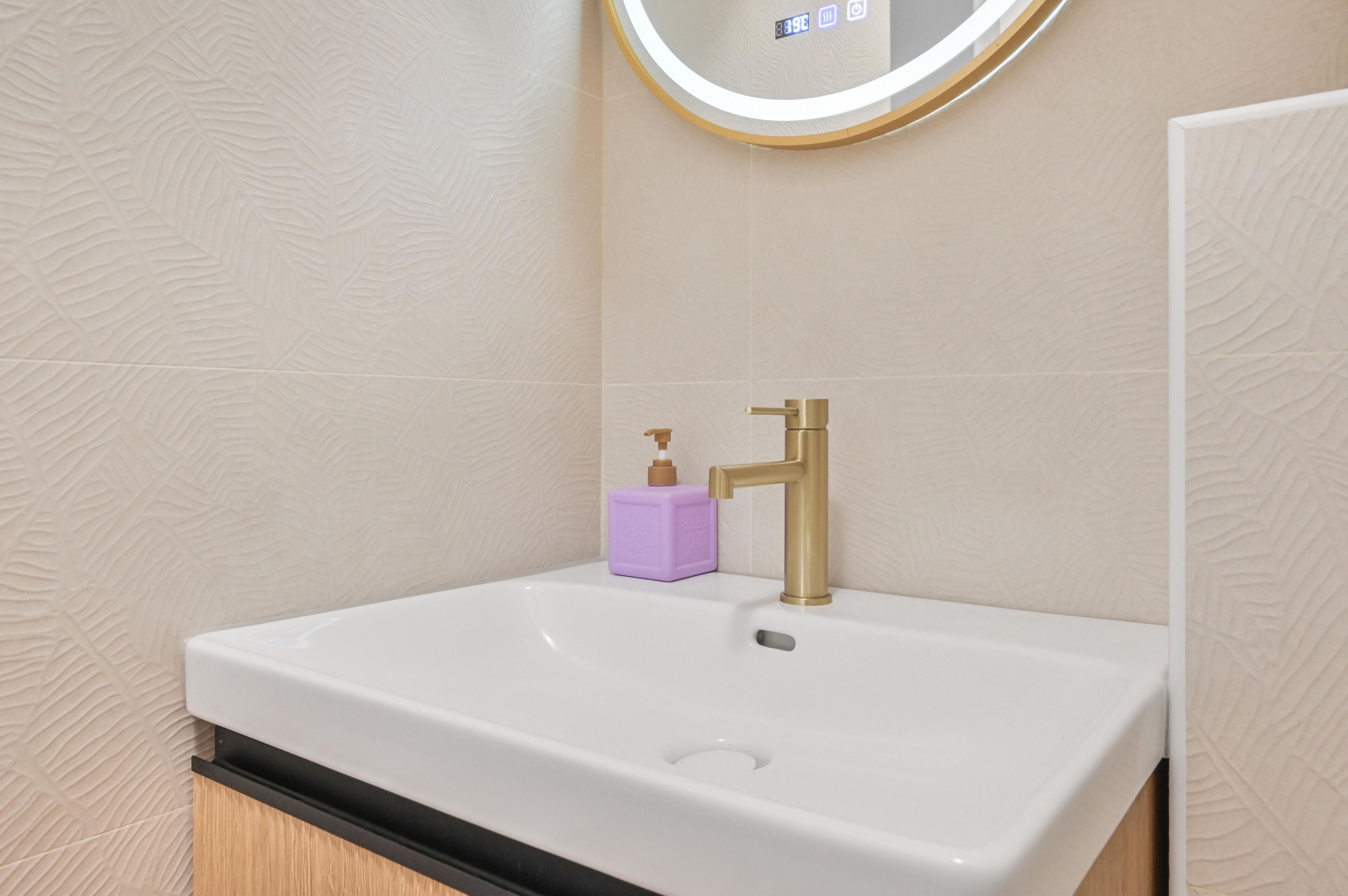 A bathroom with a white sink, gold faucet, and a purple soap dispenser.