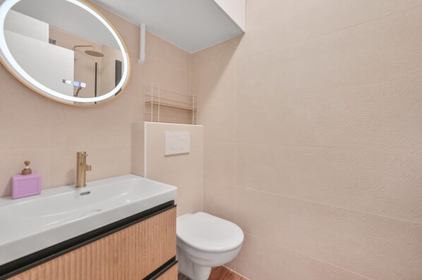 Un baño moderno con un lavamanos blanco, un espejo redondo, un inodoro y un perchero para toallas.