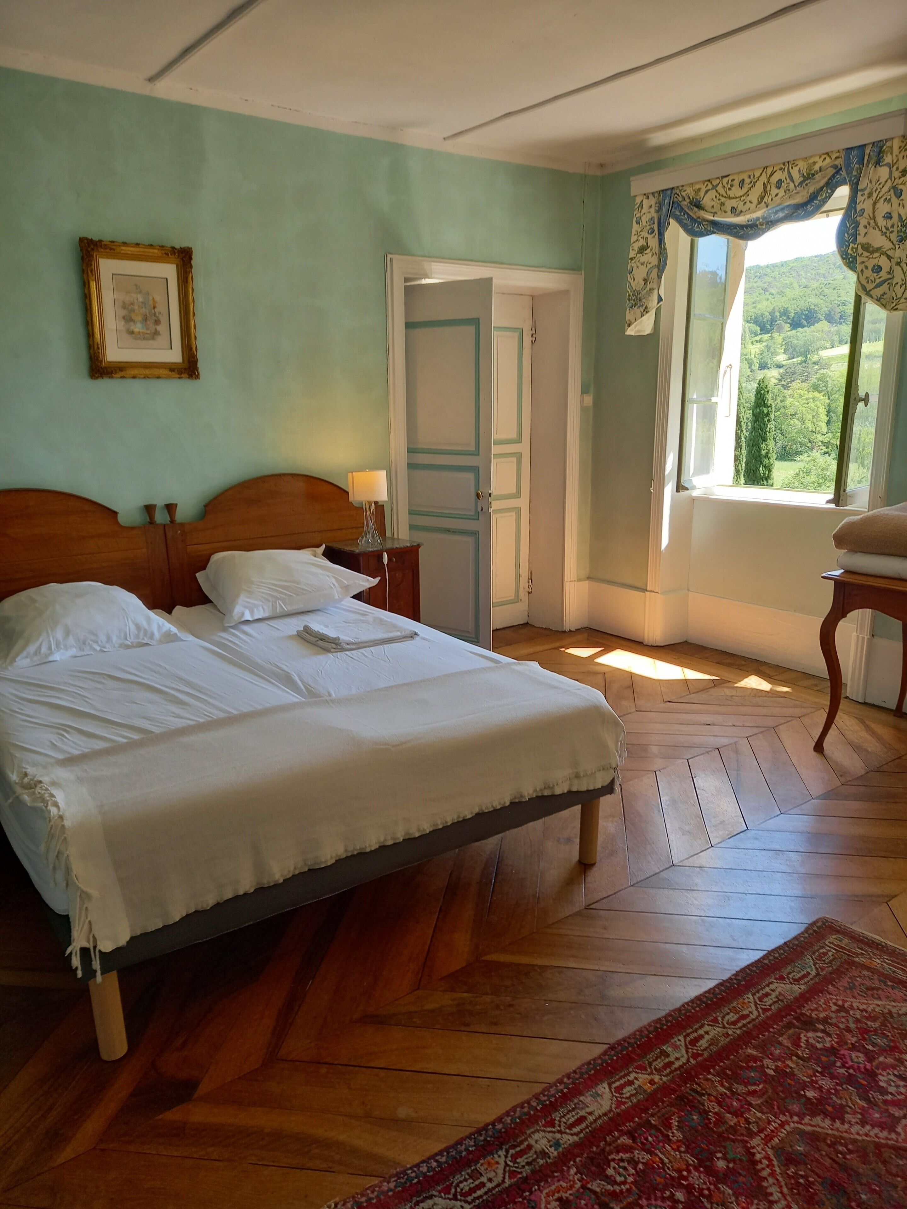 Une chambre à coucher avec un lit en bois, une table de chevet, une fenêtre avec des rideaux et une porte.