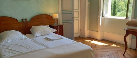 Une chambre à coucher avec un lit en bois, une table de chevet, une fenêtre avec des rideaux et une porte.