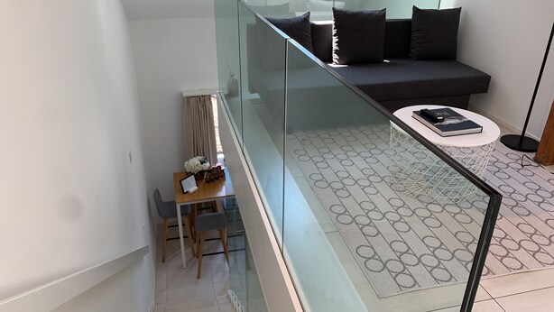 Een moderne woonkamer met glazen balustrade, een bank, een salontafel en een eethoek met stoelen en een tafel.