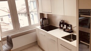 Een kleine keuken met witte kasten, een zwarte kookplaat en een raam met uitzicht op een woonwijk.