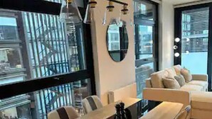 Ein moderner Essbereich mit einem langen Holztisch und Stühlen, großen Fenstern mit Stadtblick und minimalistischer Einrichtung.