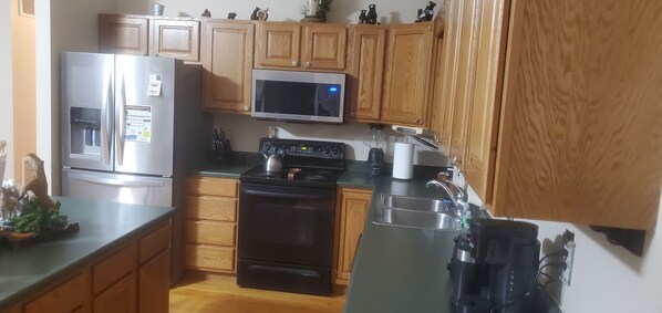 Una cocina con armarios de madera, un refrigerador de acero inoxidable, un microondas, una estufa y un lavamanos.