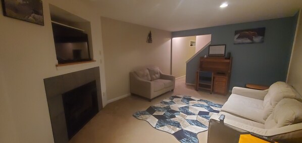 Una sala de estar con chimenea, un sofá, un tapete estampado y una escalera que sube a otra habitación.